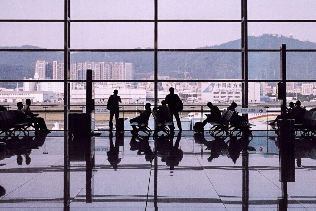 Silhouetted travelers in a modern airport terminal with large glass windows and waiting area.