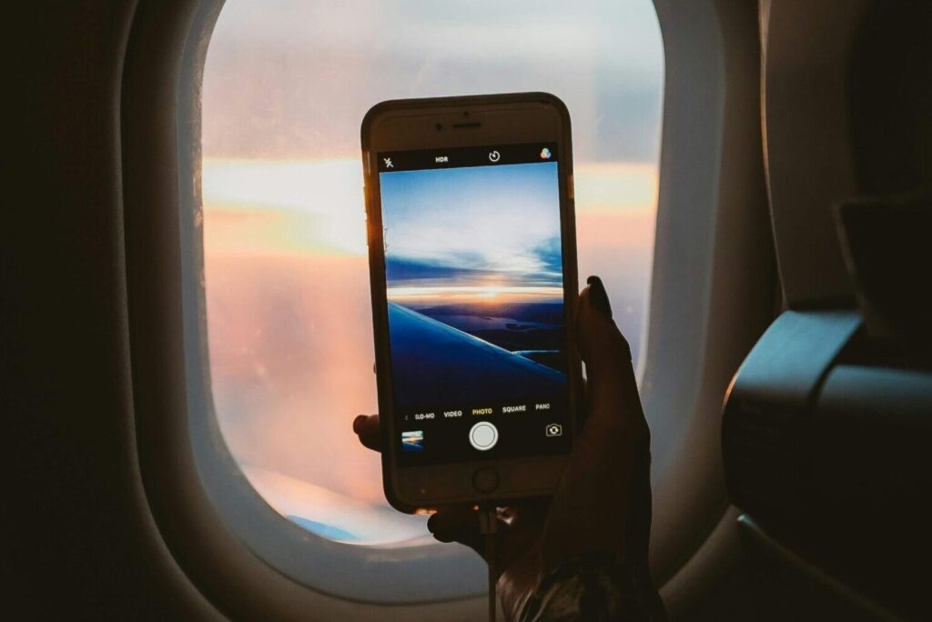 About The Calm Cabin. A person takes a photo of a sunset through an airplane window using a smartphone.